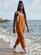Woman in a rust-orange striped jumpsuit walking along the beach shoreline