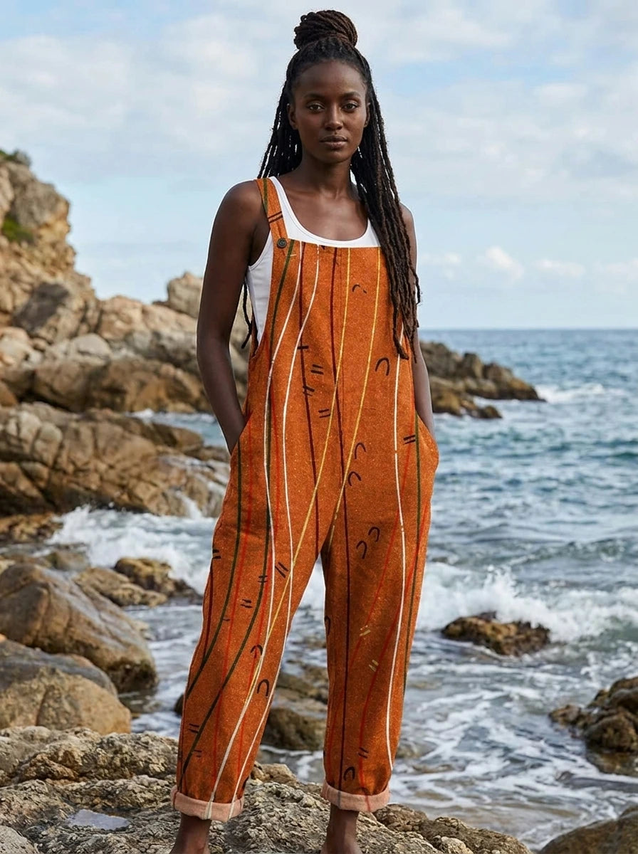 Woman wearing a rust-orange sleeveless jumpsuit with a white line print on a rocky beach