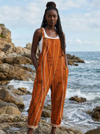 Woman wearing a rust-orange sleeveless jumpsuit with a white line print on a rocky beach