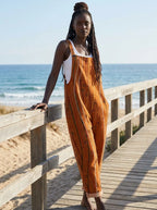 Woman in a rust-orange striped jumpsuit standing on a wooden beach boardwalk