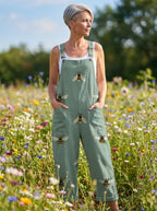 Woman wearing a sage-green bee print sleeveless wide-leg overall jumpsuit standing in a flower field