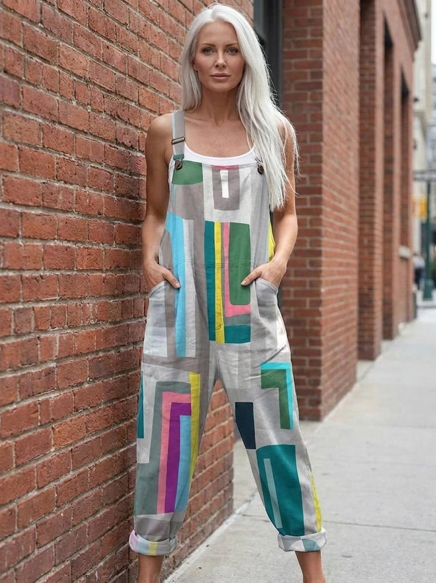 Woman wearing a grey multicolor geometric color-block wide-leg overall jumpsuit leaning against a brick wall