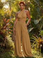 Woman wearing a camel cross halter wide-leg jumpsuit in a tropical garden