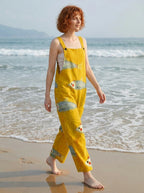 Woman wearing a mustard-yellow fish print sleeveless overall jumpsuit walking along the shoreline