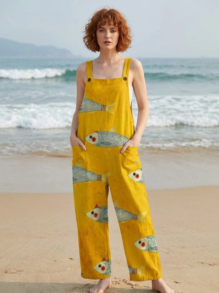 Woman wearing a mustard-yellow fish print sleeveless overall jumpsuit standing on a sandy beach