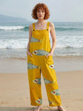 Woman wearing a mustard-yellow fish print sleeveless overall jumpsuit standing on a sandy beach