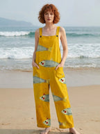 Woman wearing a mustard-yellow fish print sleeveless overall jumpsuit standing on a sandy beach