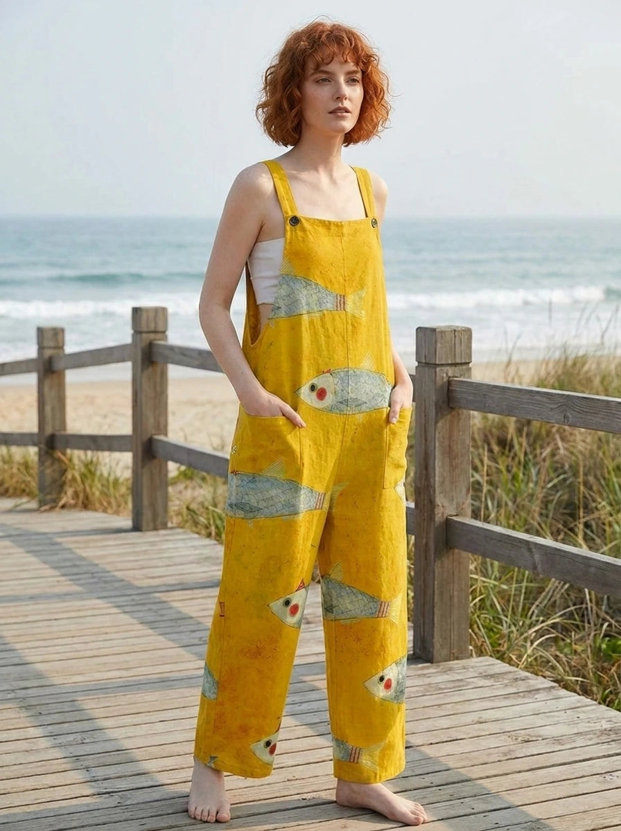 Woman wearing a mustard-yellow fish print sleeveless overall jumpsuit standing on a wooden beach boardwalk