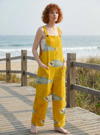 Woman wearing a mustard-yellow fish print sleeveless overall jumpsuit standing on a wooden beach boardwalk