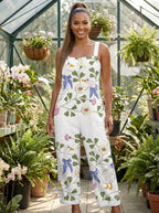 Woman wearing a white purple and blue floral print sleeveless wide-leg overall jumpsuit standing in a greenhouse