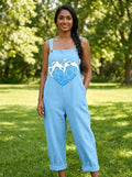 Woman wearing a light-blue heart print sleeveless overall jumpsuit standing in a green park