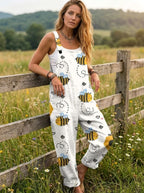 Woman wearing a white honeybee print sleeveless button-down overall jumpsuit leaning against a farm fence