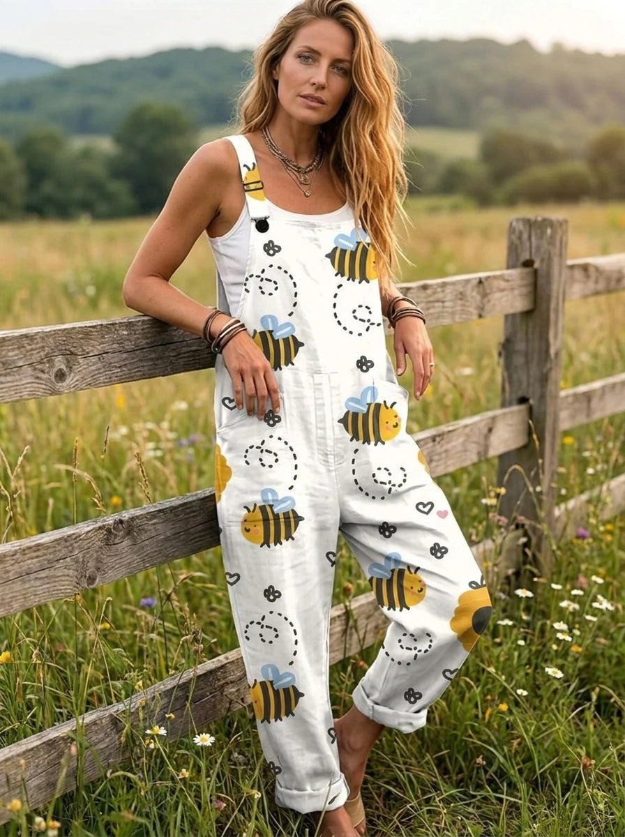 Woman wearing a white honeybee print sleeveless button-down overall jumpsuit leaning against a farm fence