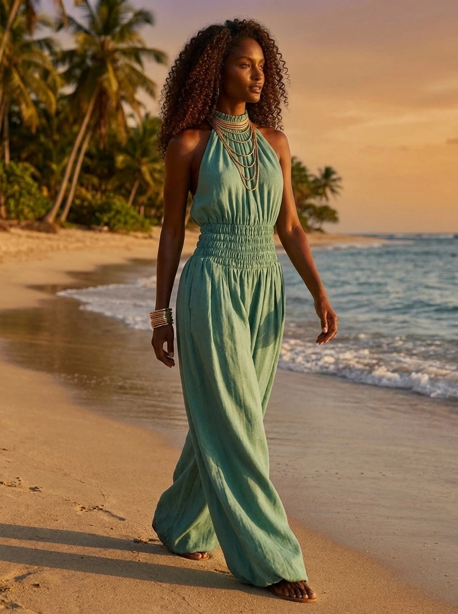 Woman wearing a green smocked-waist wide-leg palazzo jumpsuit walking on a tropical beach at golden hour