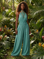Woman wearing a green smocked-waist wide-leg palazzo jumpsuit in a lush tropical garden