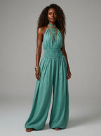 Woman wearing a green smocked-waist wide-leg palazzo jumpsuit in a studio setting