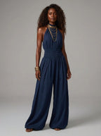 Woman wearing a navy blue smocked-waist wide-leg palazzo jumpsuit in a studio setting