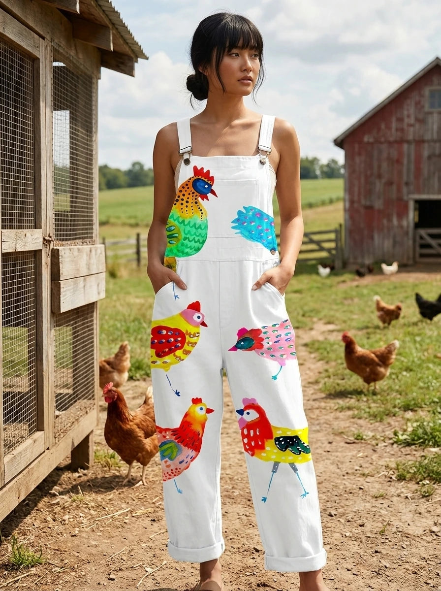 Woman wearing a white colorful rooster and bird print sleeveless wide-leg overall jumpsuit near a chicken coop