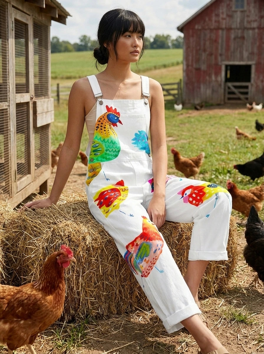 Woman wearing a white colorful rooster and bird print sleeveless wide-leg overall jumpsuit sitting on hay bales