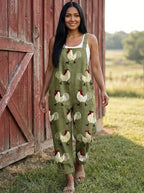 Woman wearing an olive-green rooster print wide-leg overall jumpsuit standing near a red barn door