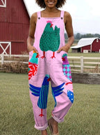Woman wearing a pink colorful rooster print sleeveless wide-leg overall jumpsuit standing near a red barn