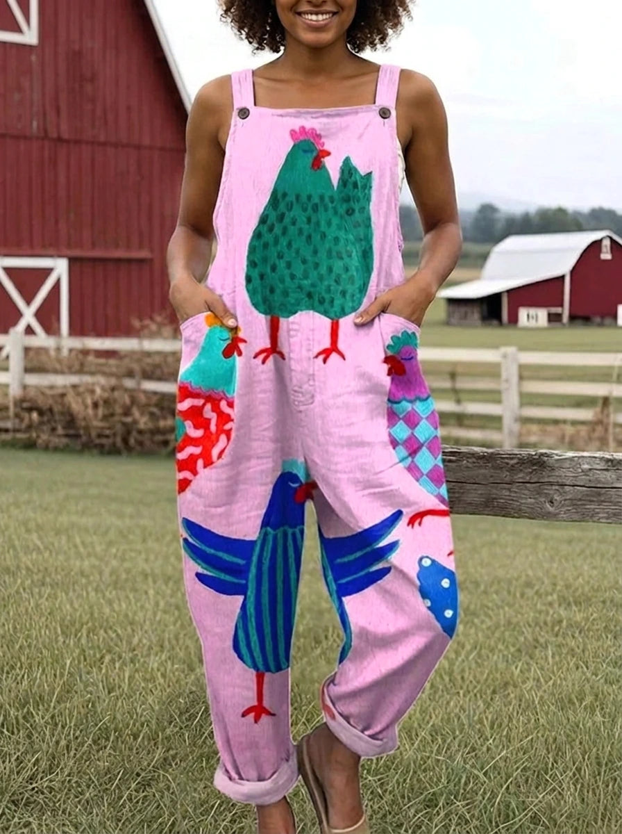 Woman wearing a pink colorful rooster print sleeveless wide-leg overall jumpsuit standing near a red barn