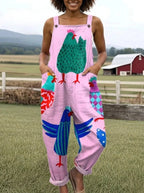 Woman wearing a pink colorful rooster print sleeveless wide-leg overall jumpsuit standing in a farm setting