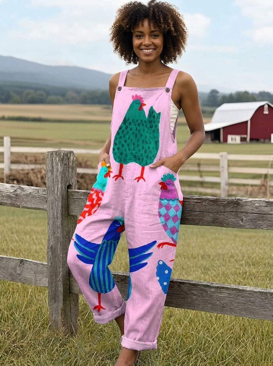 Woman wearing a pink colorful rooster print sleeveless wide-leg overall jumpsuit leaning against a wooden fence