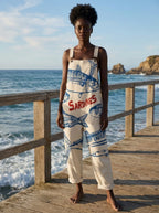 Woman in a cream sardine print jumpsuit standing on a wooden pier