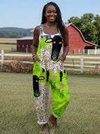 Woman wearing a green sheep and floral print sleeveless wide-leg overall jumpsuit standing in a farm field