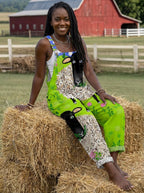 Woman wearing a green sheep and floral print sleeveless wide-leg overall jumpsuit sitting on hay bales