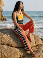 Woman sitting on a large beach rock wearing a striped color-block jumpsuit