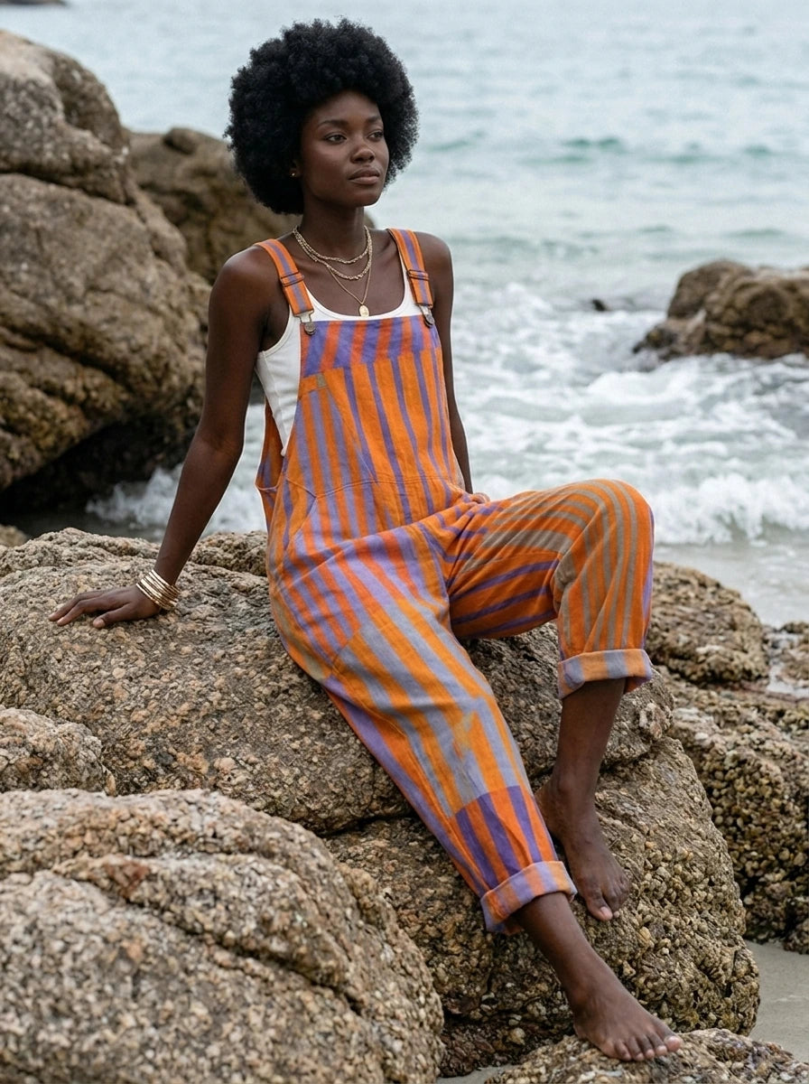 Woman sitting on beach rocks wearing a sunset print jumpsuit