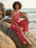 Woman sitting on beach rocks wearing a wildflower print jumpsuit
