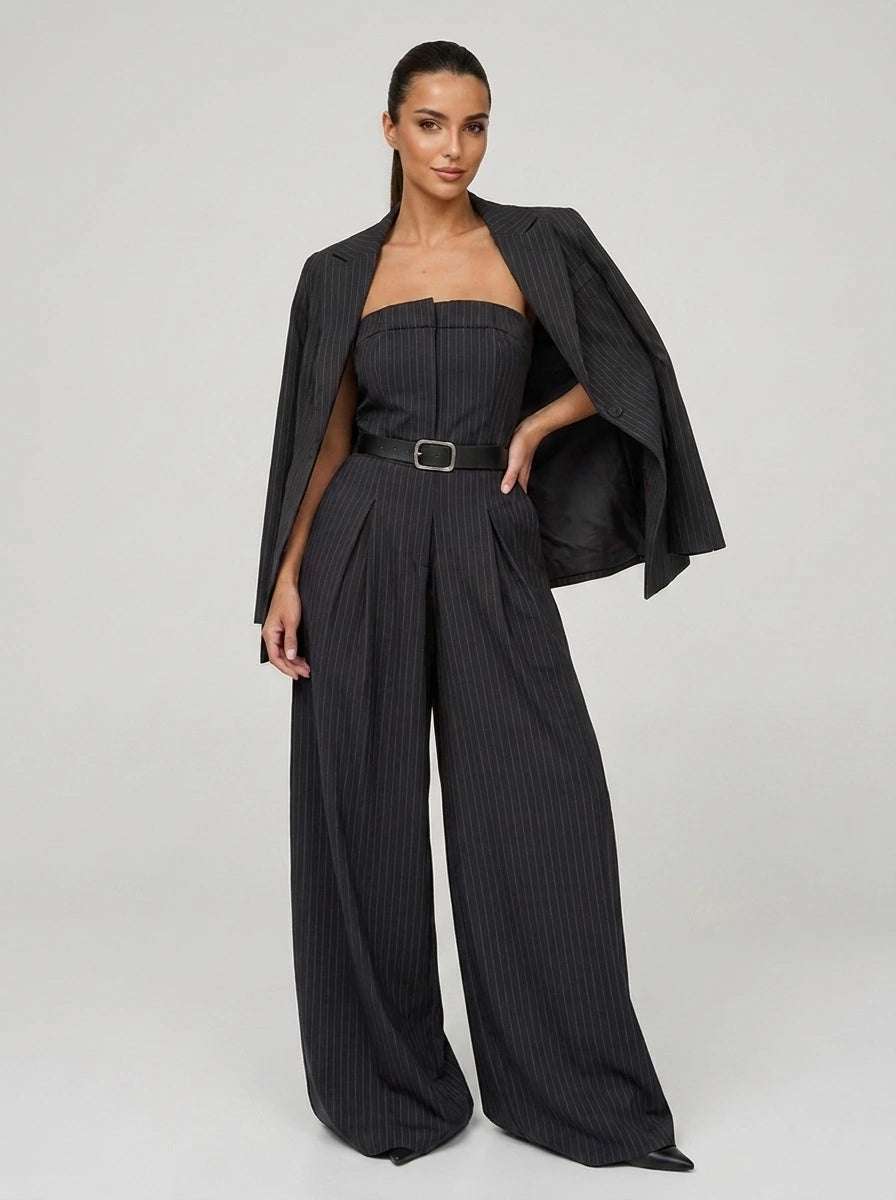 Woman wearing a dark charcoal grey pinstripe wide-leg jumpsuit with matching blazer, studio shot