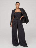 Woman wearing a dark charcoal grey pinstripe wide-leg jumpsuit with matching blazer, studio shot
