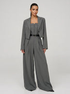 Woman wearing a grey wide-leg jumpsuit with matching cropped blazer, studio shot