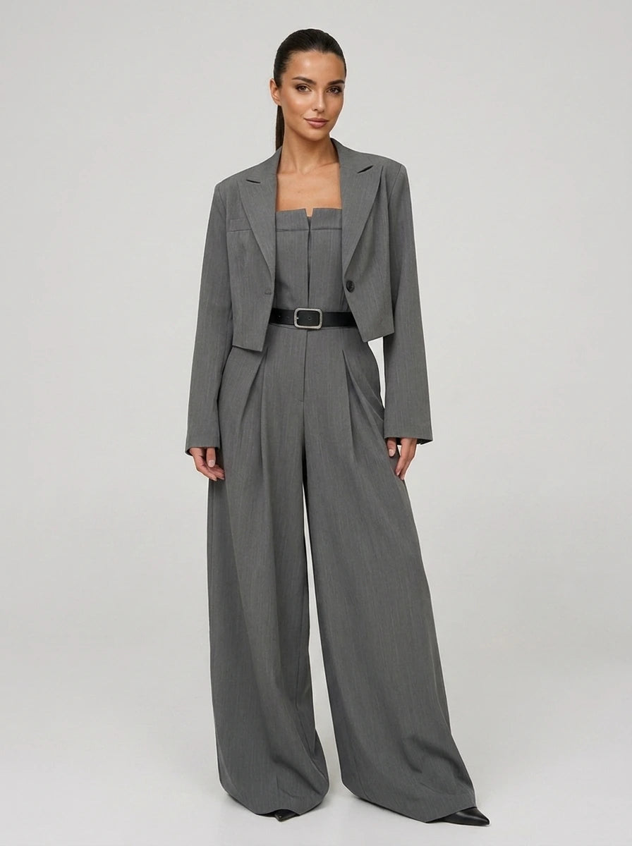 Woman wearing a grey wide-leg jumpsuit with matching cropped blazer, studio shot