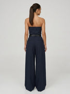 Back view of woman wearing a navy pinstripe wide-leg jumpsuit, studio shot