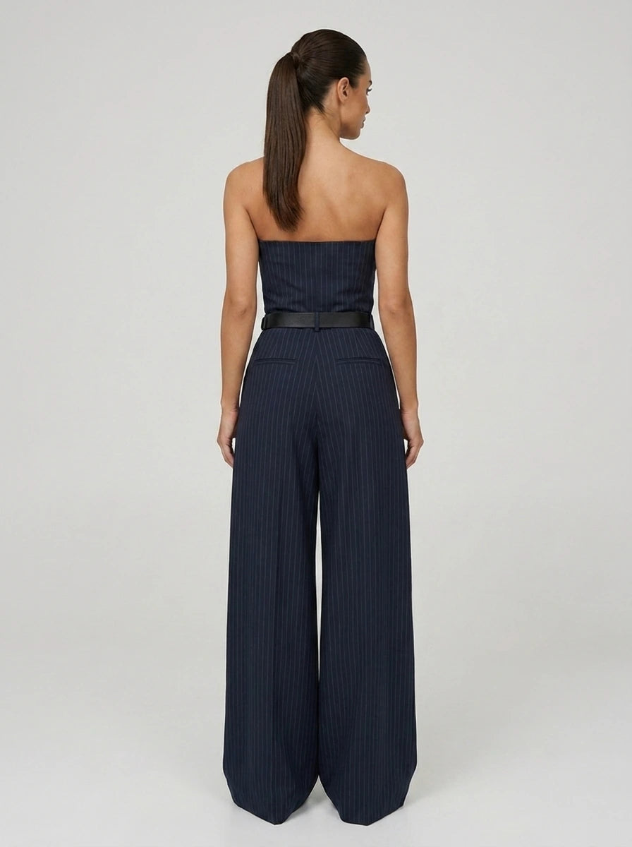 Back view of woman wearing a navy pinstripe wide-leg jumpsuit, studio shot
