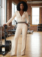 Woman wearing a beige knit zip-front jumpsuit in a bright fitness studio