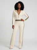 Woman wearing a beige knit zip-front jumpsuit with hood and sporty stripes, studio shot