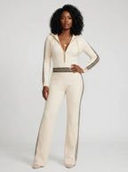 Woman wearing a beige knit zip-front jumpsuit with hood and sporty stripes, studio shot