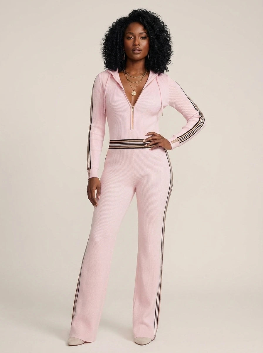 Woman wearing a pink knit zip-front jumpsuit with hood and sporty stripes, studio shot