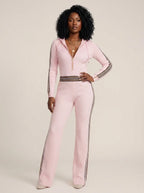 Woman wearing a pink knit zip-front jumpsuit with hood and sporty stripes, studio shot