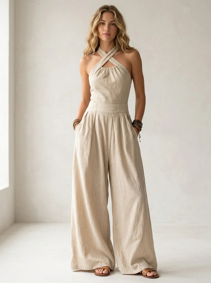 Driftly beige crossed halter wrap jumpsuit with fluid wide-leg trousers and a defined waist, in a minimalist studio setting with soft window light.