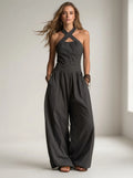 Driftly black crossed halter wrap jumpsuit with fluid wide-leg trousers and a defined waist, in a minimalist studio setting with soft window light.