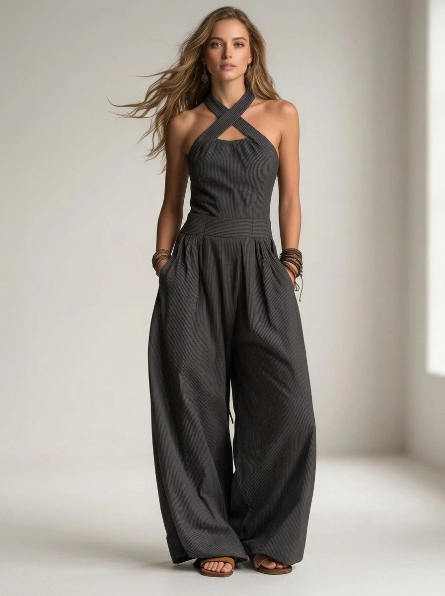 Driftly black crossed halter wrap jumpsuit with fluid wide-leg trousers and a defined waist, in a minimalist studio setting with soft window light.