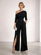Driftly black asymmetrical one-shoulder jumpsuit with crossed detail and flowing wide-leg trousers, in a minimalist studio setting with soft window light.