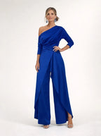 Driftly blue asymmetrical one-shoulder jumpsuit with crossed detail and flowing wide-leg trousers, in a minimalist studio setting with soft window light.